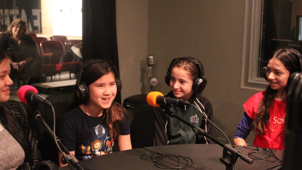 Three teens wearing headphones speaking into microphones in a radio studio