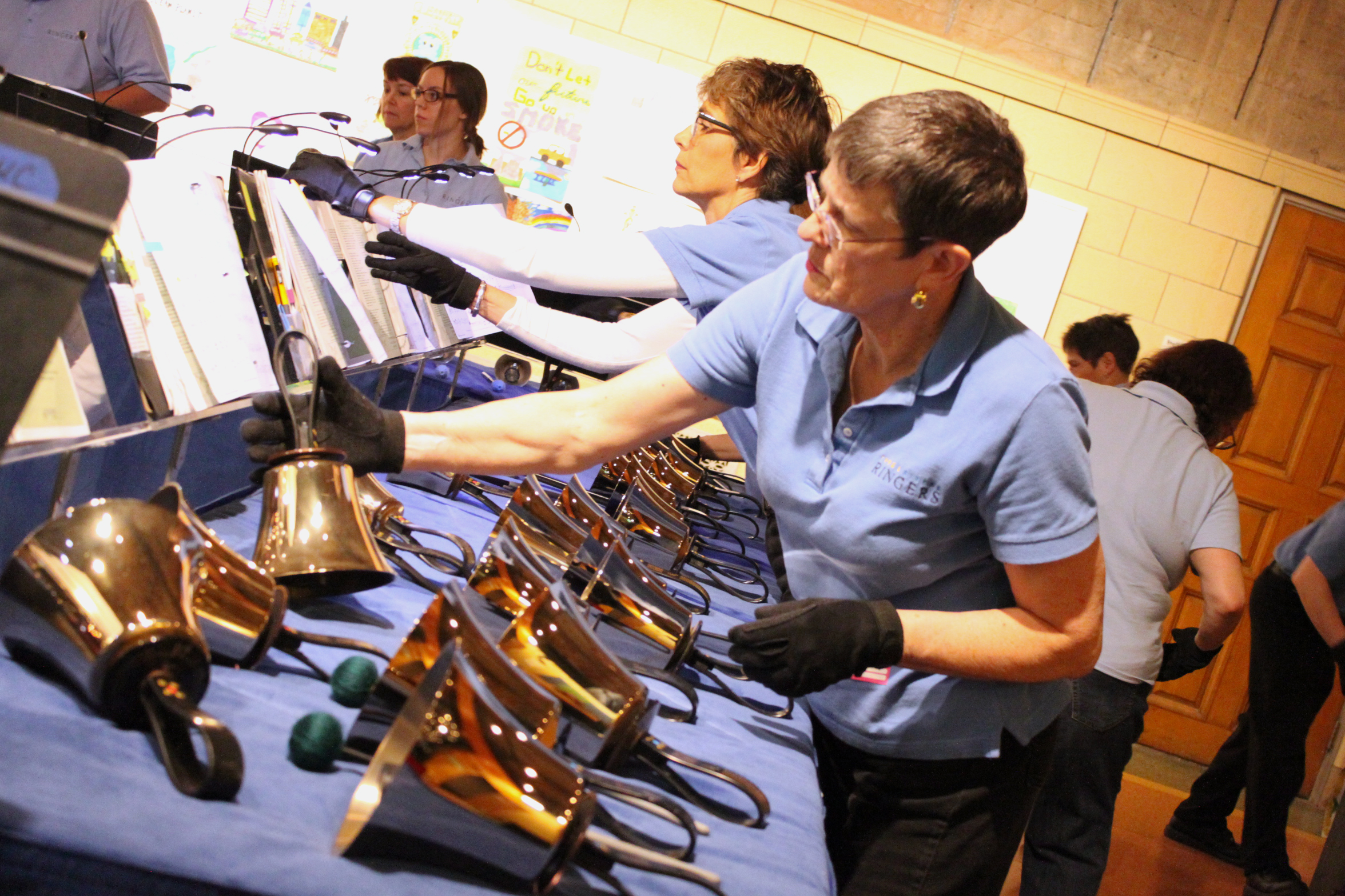 Four adults standing behind a large collection of handbells looking at sheet music on music stands