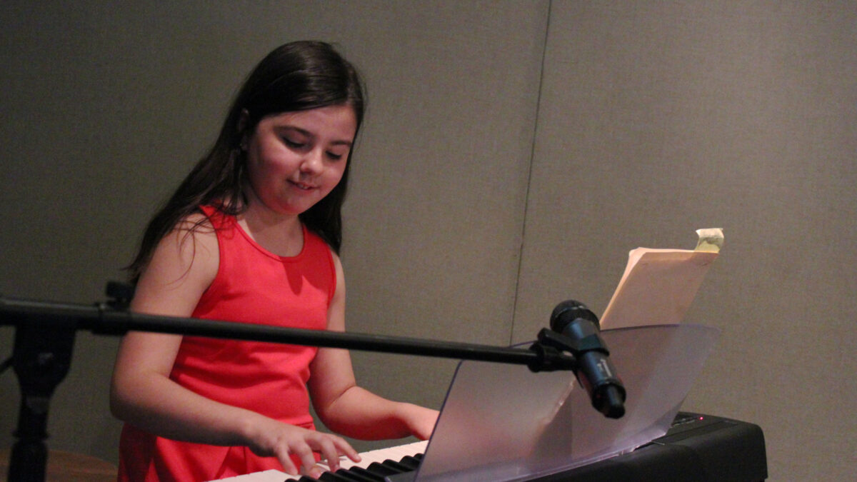 A youth playing a piano keyboard sitting behind a microphone in a radio studio