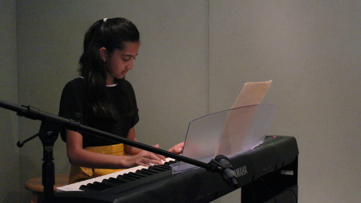 A youth playing a piano keyboard sitting behind a microphone in a radio studio