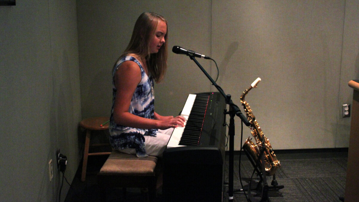 A teen playing a piano keyboard and singing into a microphone in a radio studio