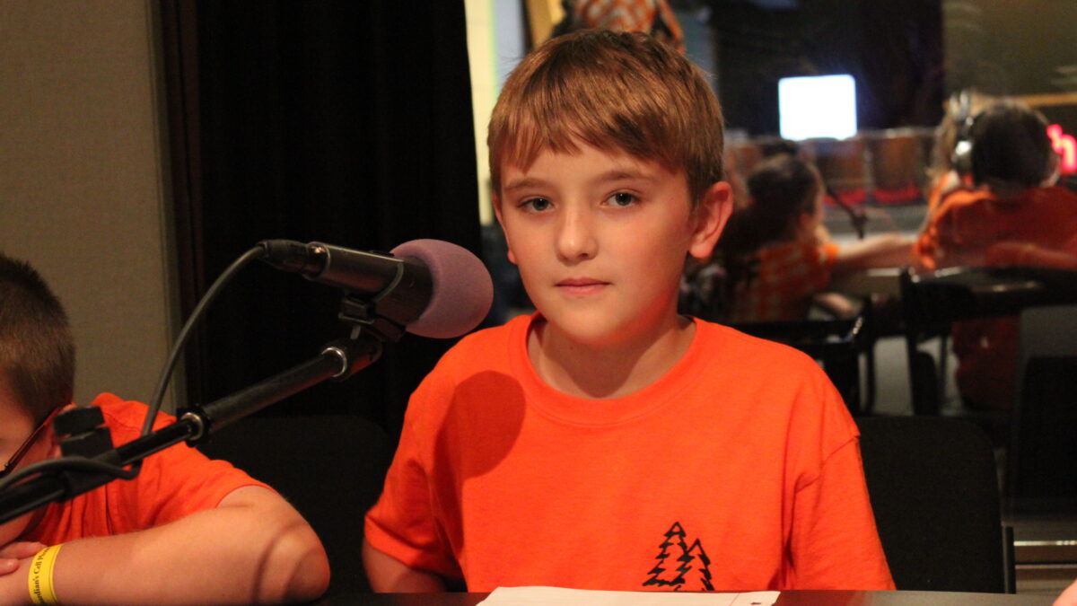 A youth sitting behind a microphone in a radio studio