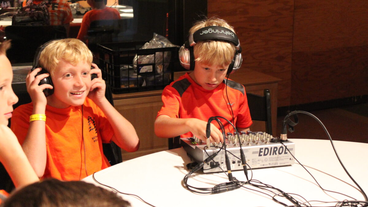Two youth wearing headphones, one interacting with a mixing board