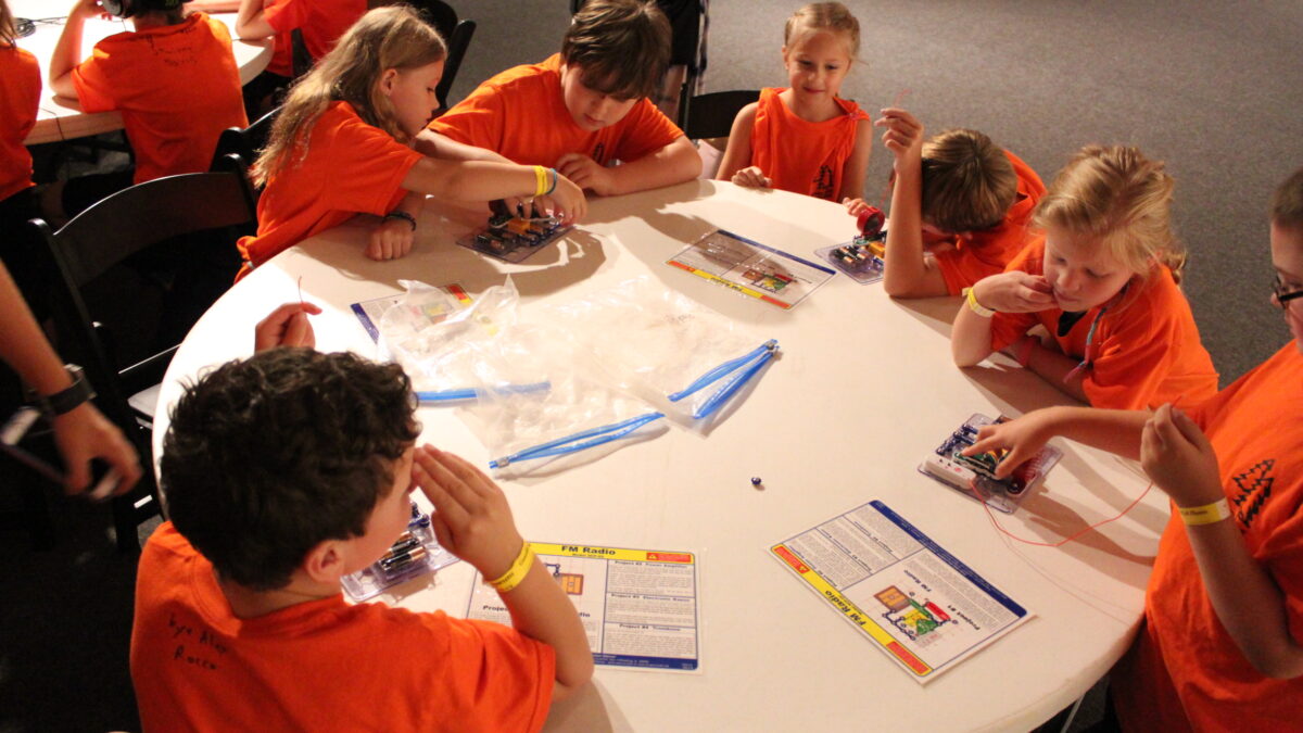 Seven youth sitting around a white round table playing with snap circuits