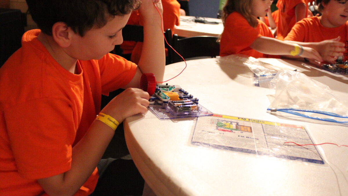 Three youth sitting around a white round table playing with snap circuits
