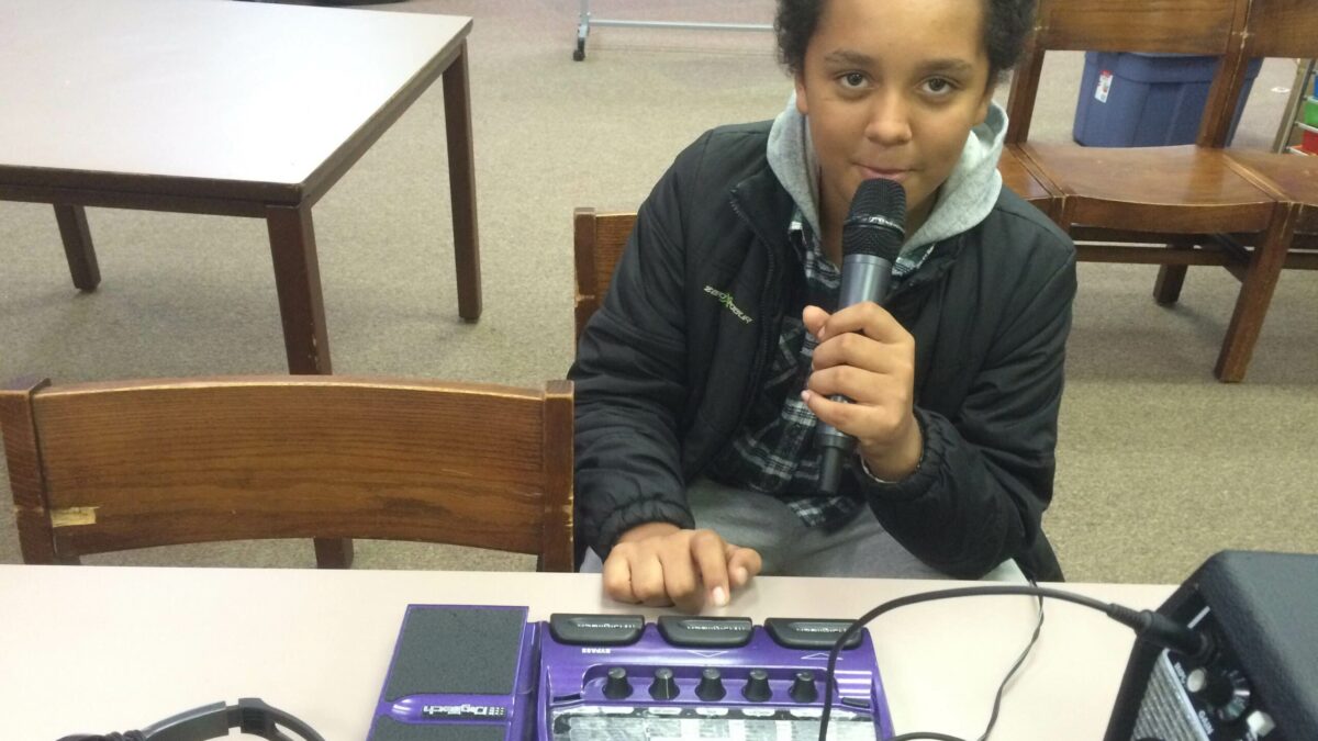 A youth holding and speaking into a microphone sitting in a library