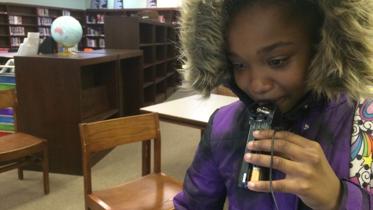 A youth holding a portable recorder in a library