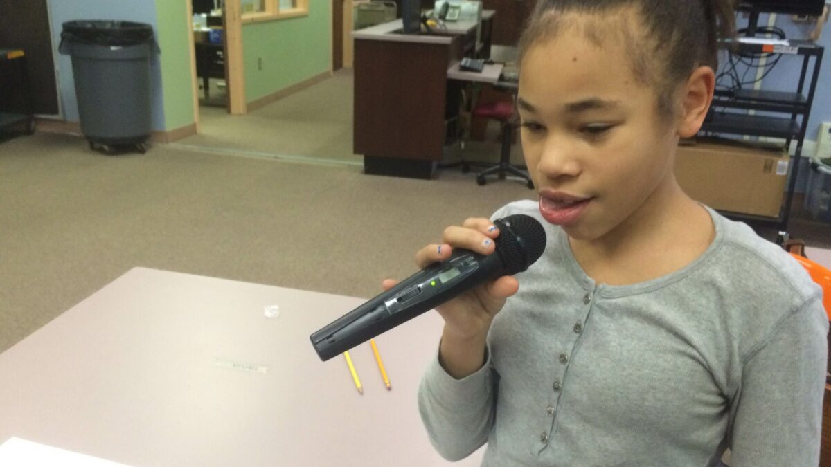 A youth holding and speaking into a microphone in a library