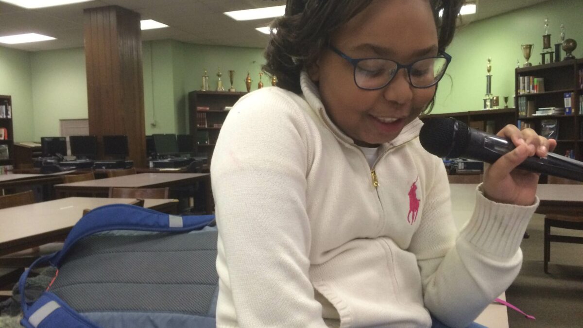 A youth looking down and holding and speaking into a microphone in a library