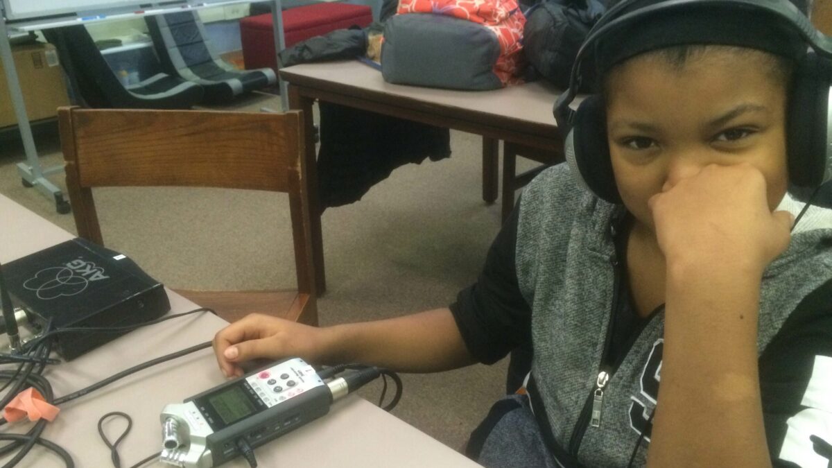 A youth wearing headphones listening to a portable recorder on a table
