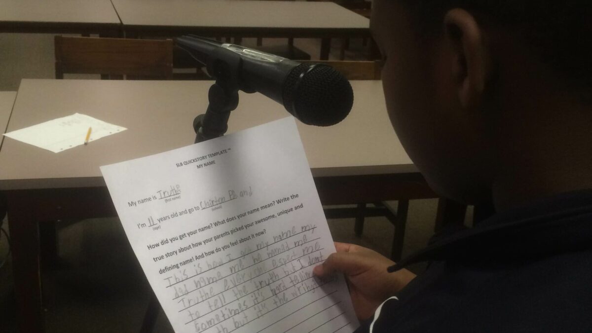 A youth reading from a piece of paper into a microphone in a library