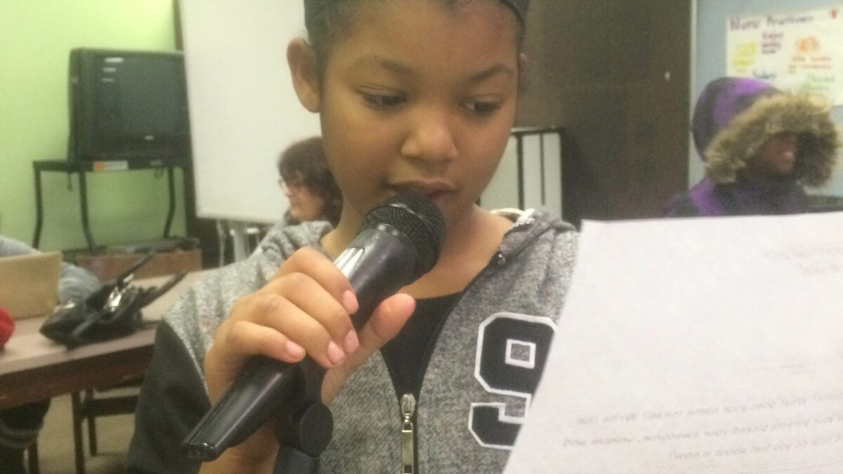 A youth reading from a piece of paper into a microphone