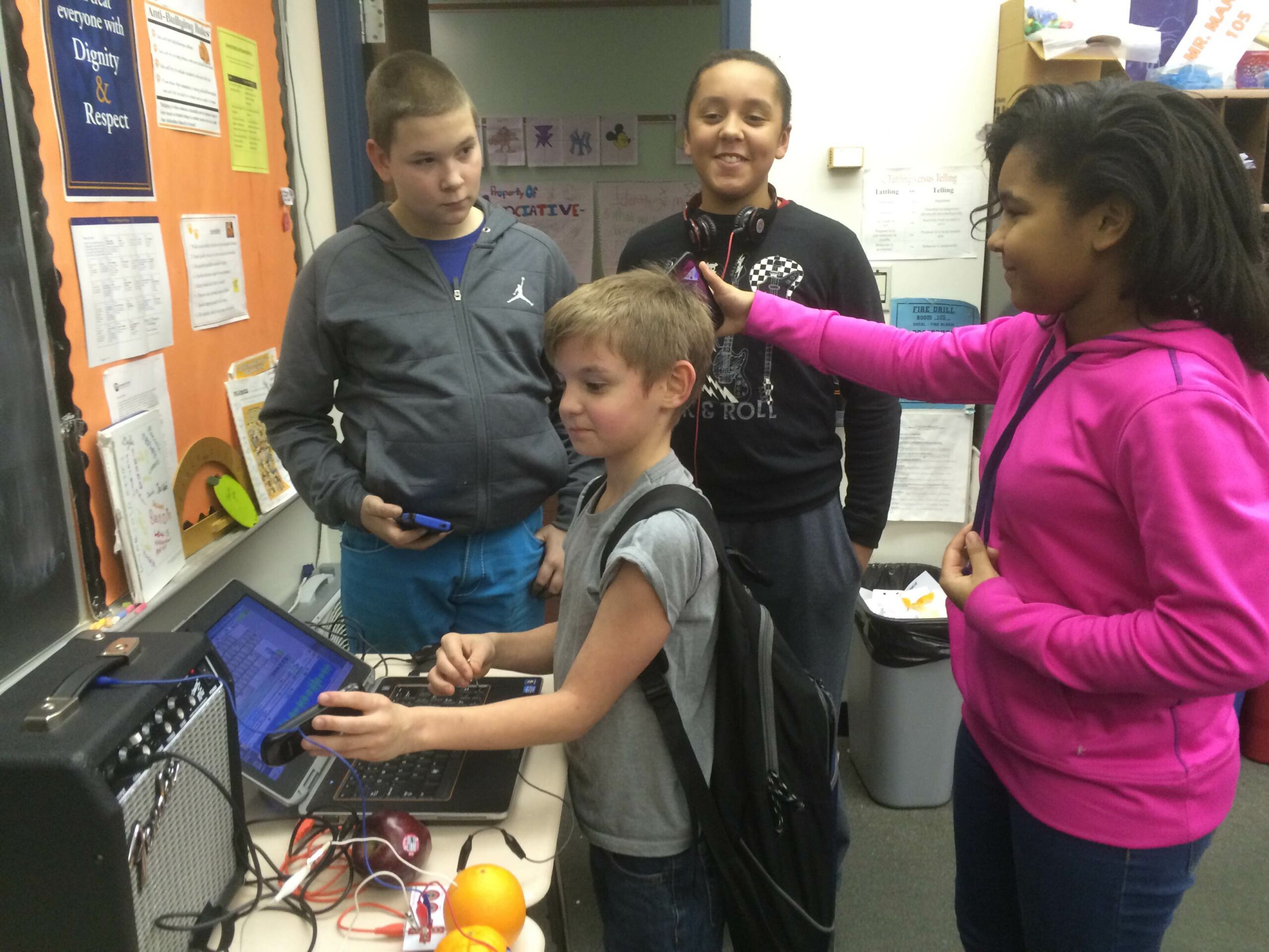 Four youth standing in front of a laptop computer in a classroom