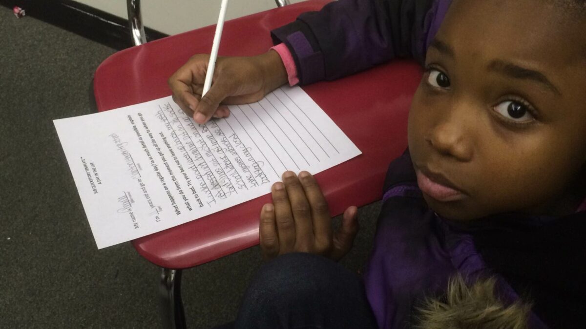 A youth writing on a piece of paper on a classroom chair