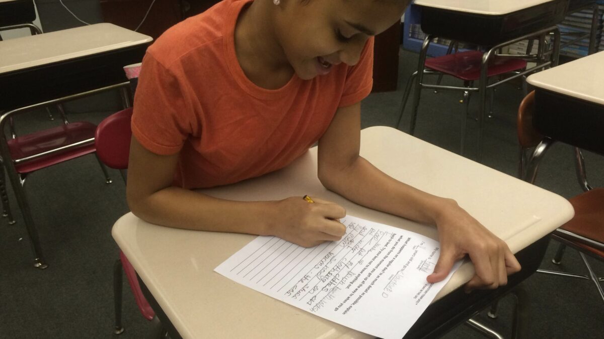 A youth writing onto a piece of paper on a classroom desk