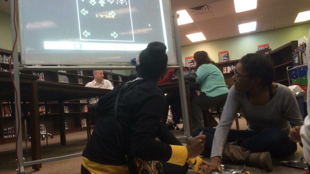 Two youth putting their hands on a piece of tinfoil while looking at a screen on a projector
