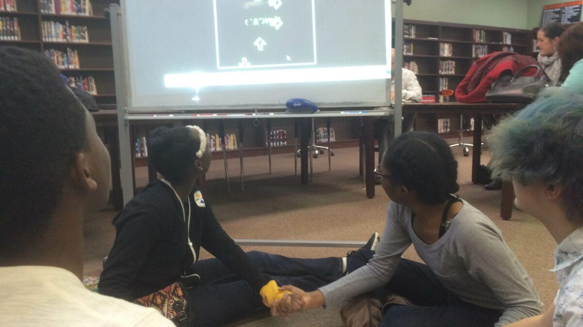 Four youth holding hands surrounding tinfoil looking at a projected screen