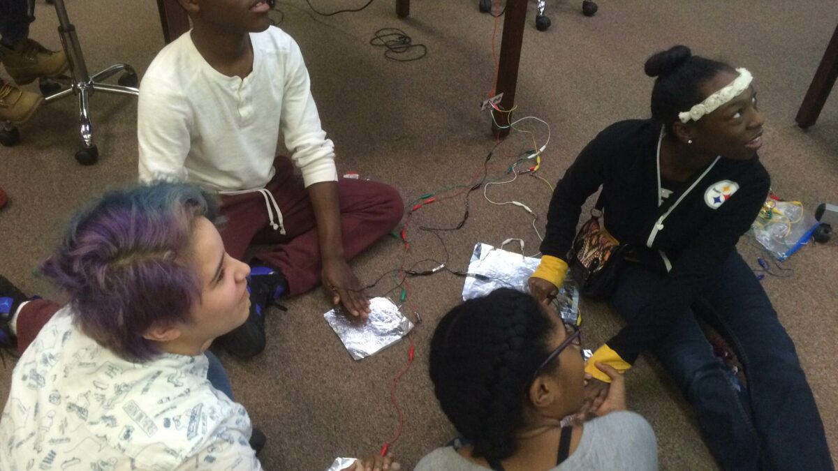 Four youth sitting in a circle putting their hands on tinfoil