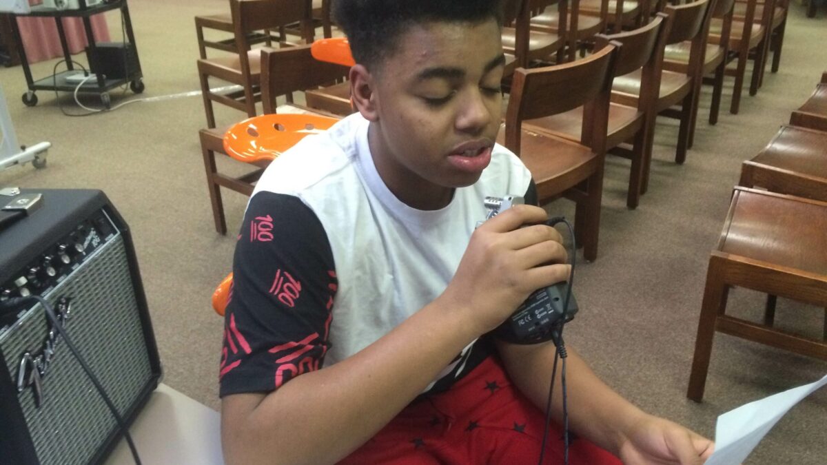 A youth reading a piece of paper speaking into a portable recorder in a library
