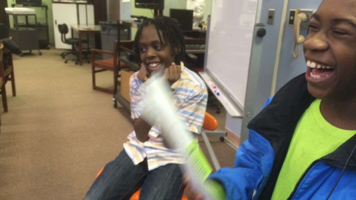 Two youth, one holding a piece of paper, laughing in a library