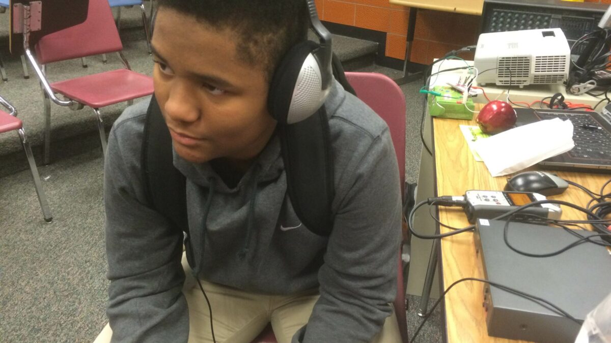 IMG_2308 A youth wearing headphones connected to a portable recorder on a wooden desk in a classroom