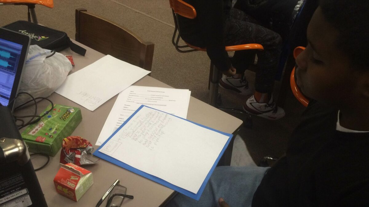 A youth looking down at a piece of paper on a table with other pieces of paper, snacks and a juice box