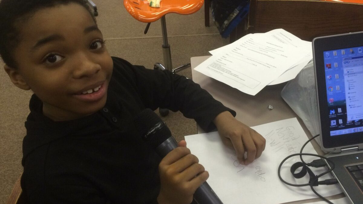 A youth holding a microphone sitting next to a laptop