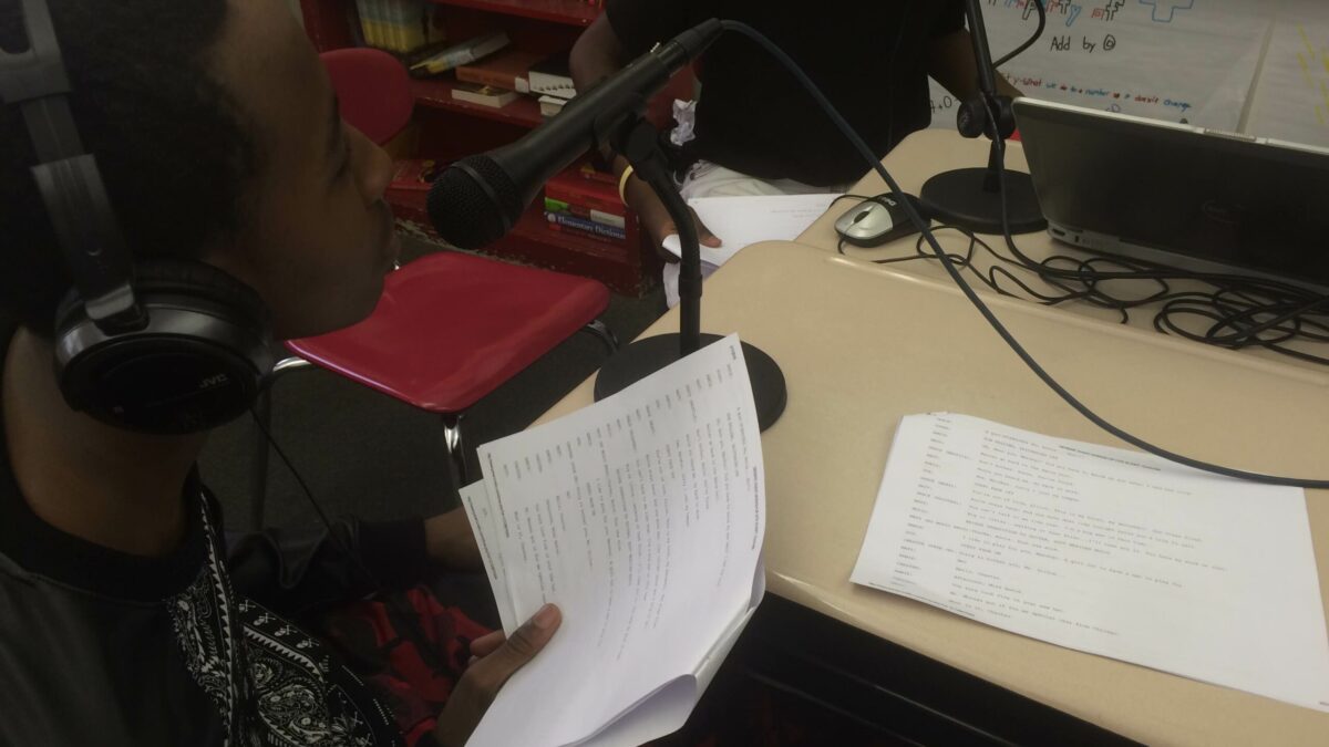 A youth wearing headphones reading a piece of paper into a microphone