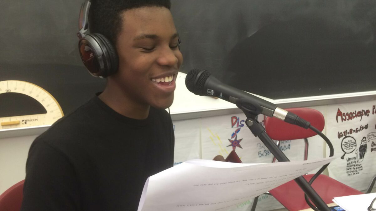 A youth wearing headphones reading from a piece of paper into a microphone