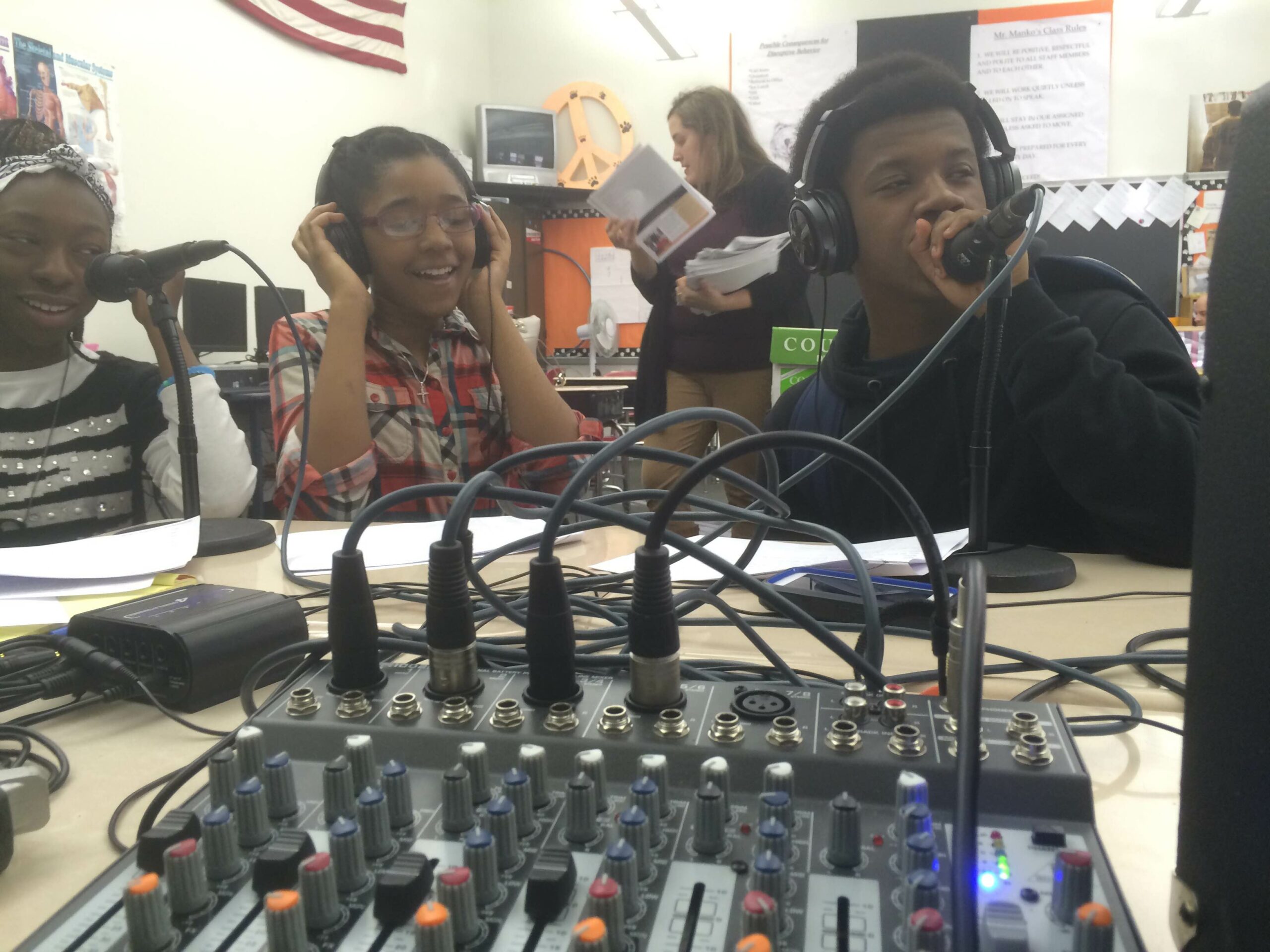 Three youth wearing headphones speaking into microphones connected to a mixer