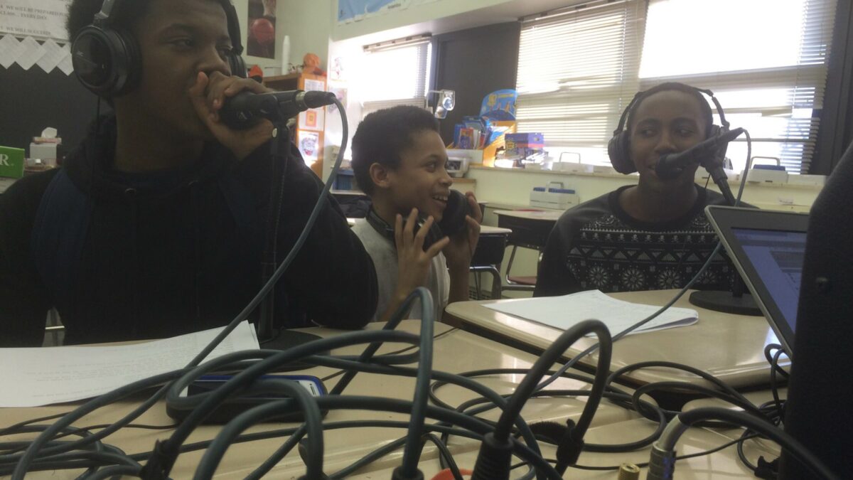 Three youth wearing headphones speaking into microphones in a classroom