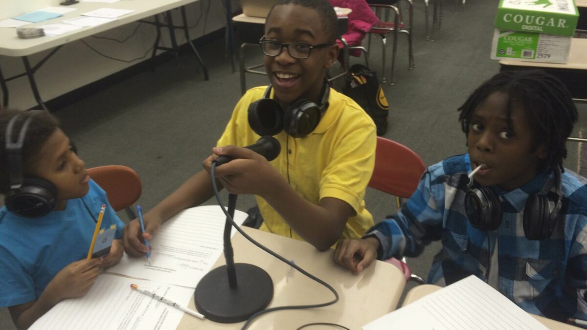 Three youth wearing headphones speaking into microphones in a classroom