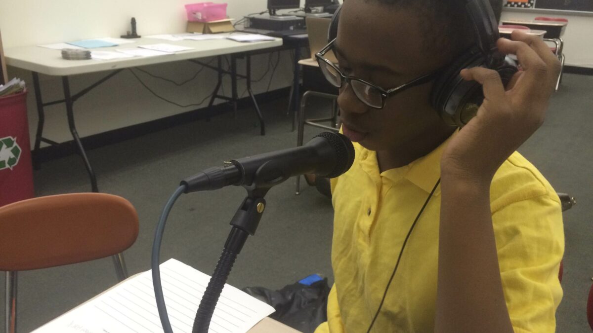 A youth wearing headphones speaking into a microphone in a classroom
