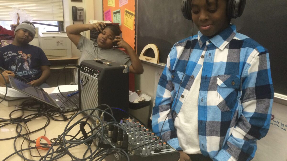 Three youth wearing headphones, one interacting with a mixer and a portable recorder