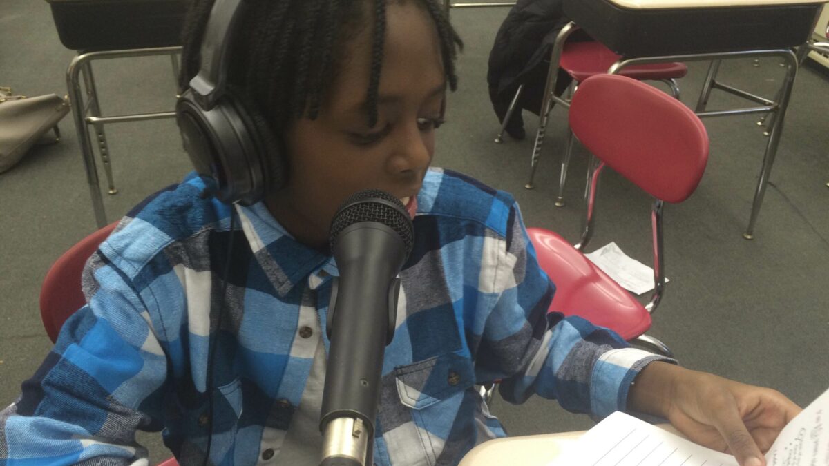 A youth wearing headphones reading from a piece of paper into a microphone
