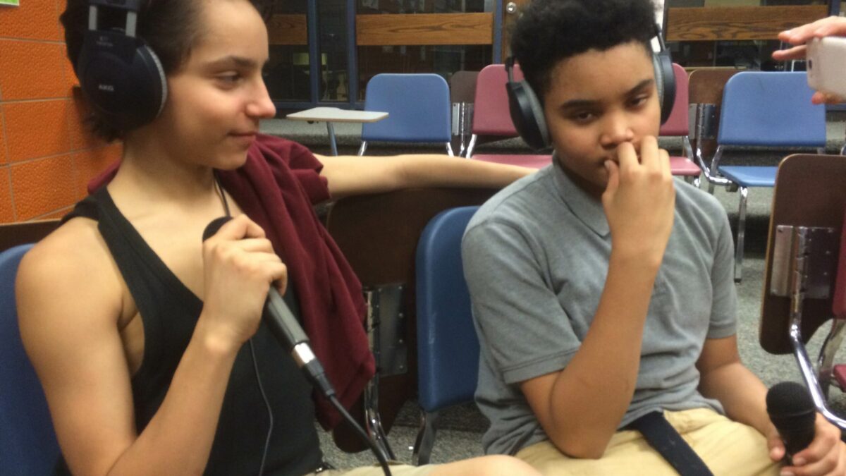 Two youth wearing headphones and holding microphones in a classroom