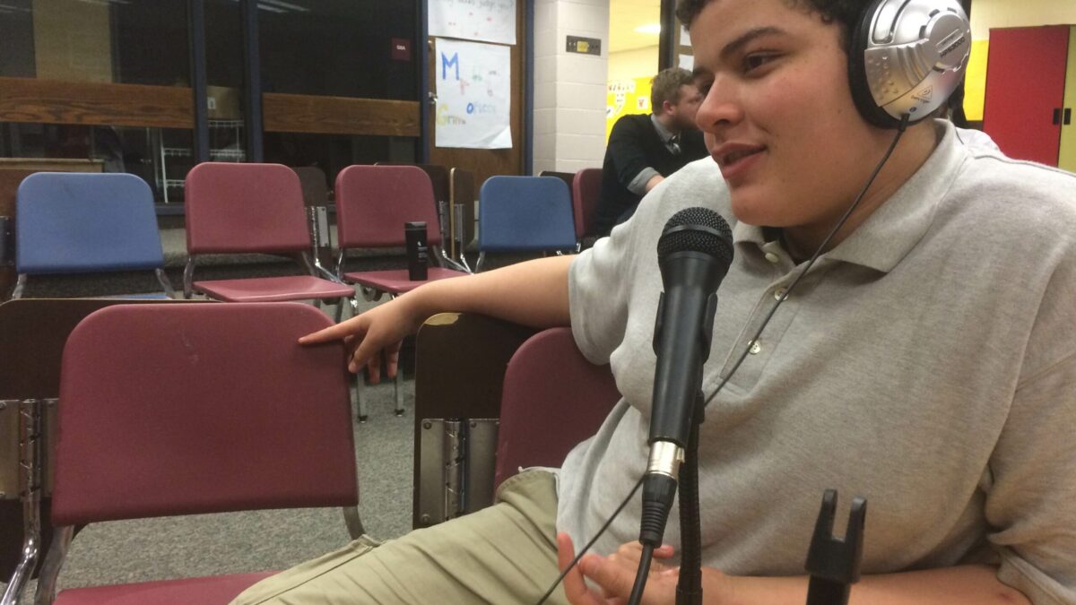 A youth wearing headphones speaking into a microphone in a classroom