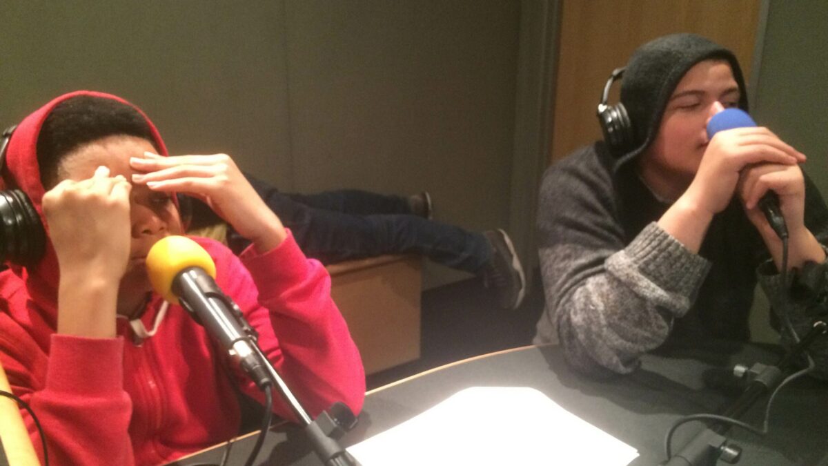 Two youth wearing headphones speaking into microphones in a radio studio