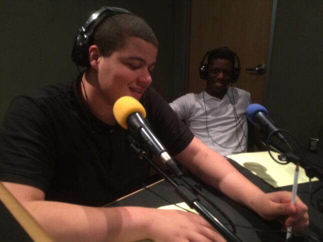 Two teens wearing headphones speaking into microphones in a radio studio