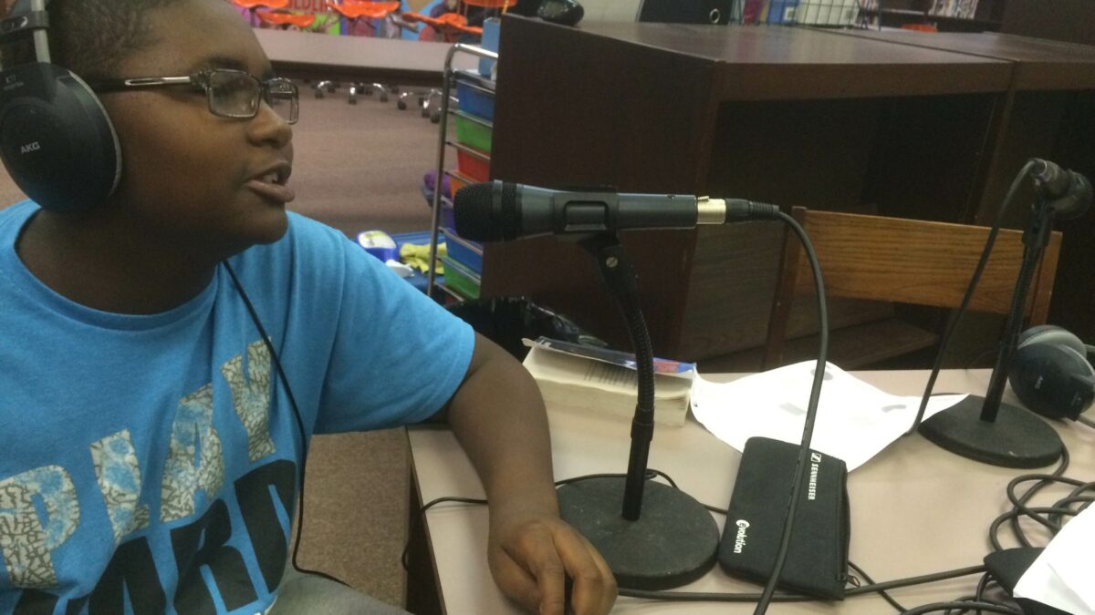 A youth wearing headphones speaking into a microphone in a library
