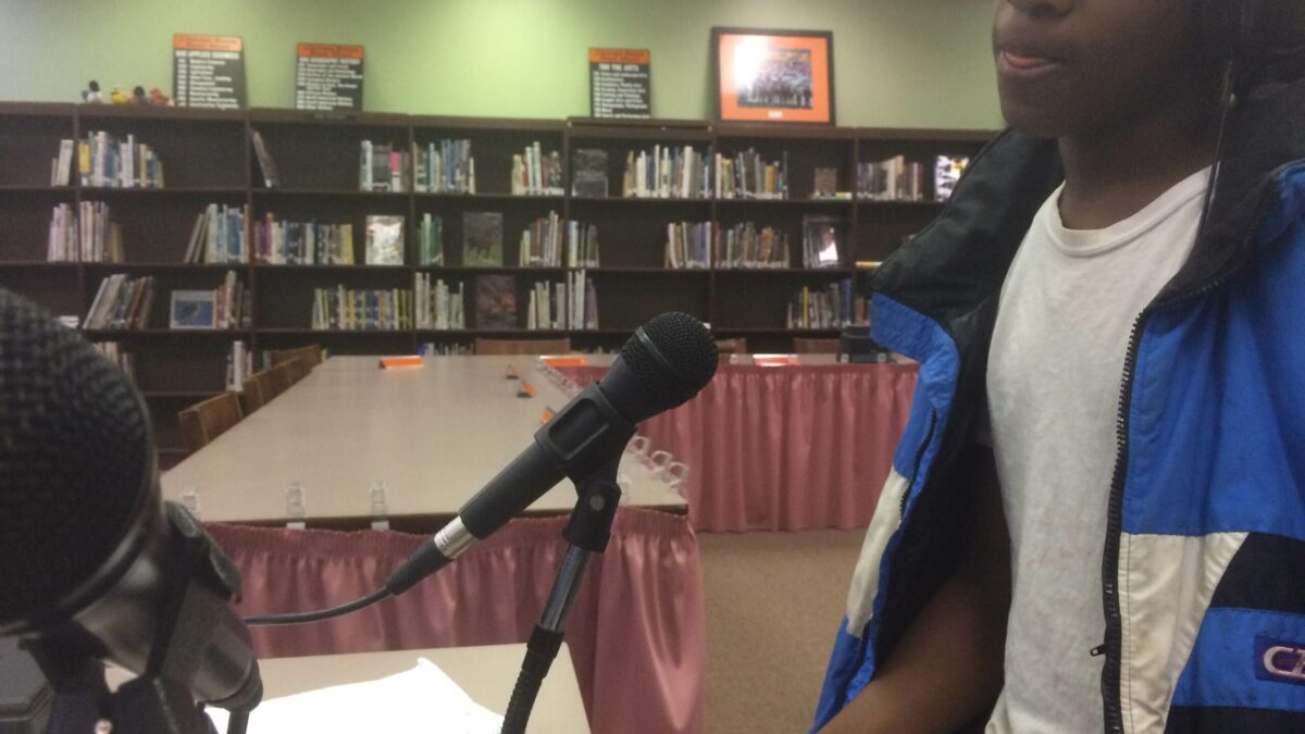 A youth wearing headphones speaking into a microphone in a library