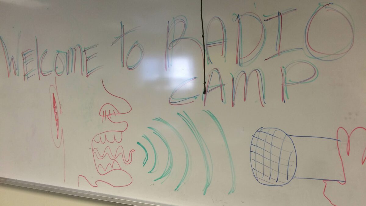 A white board with a crude drawing of a mouth screaming into a microphone, and the text "Welcome to RADIO CAMP"