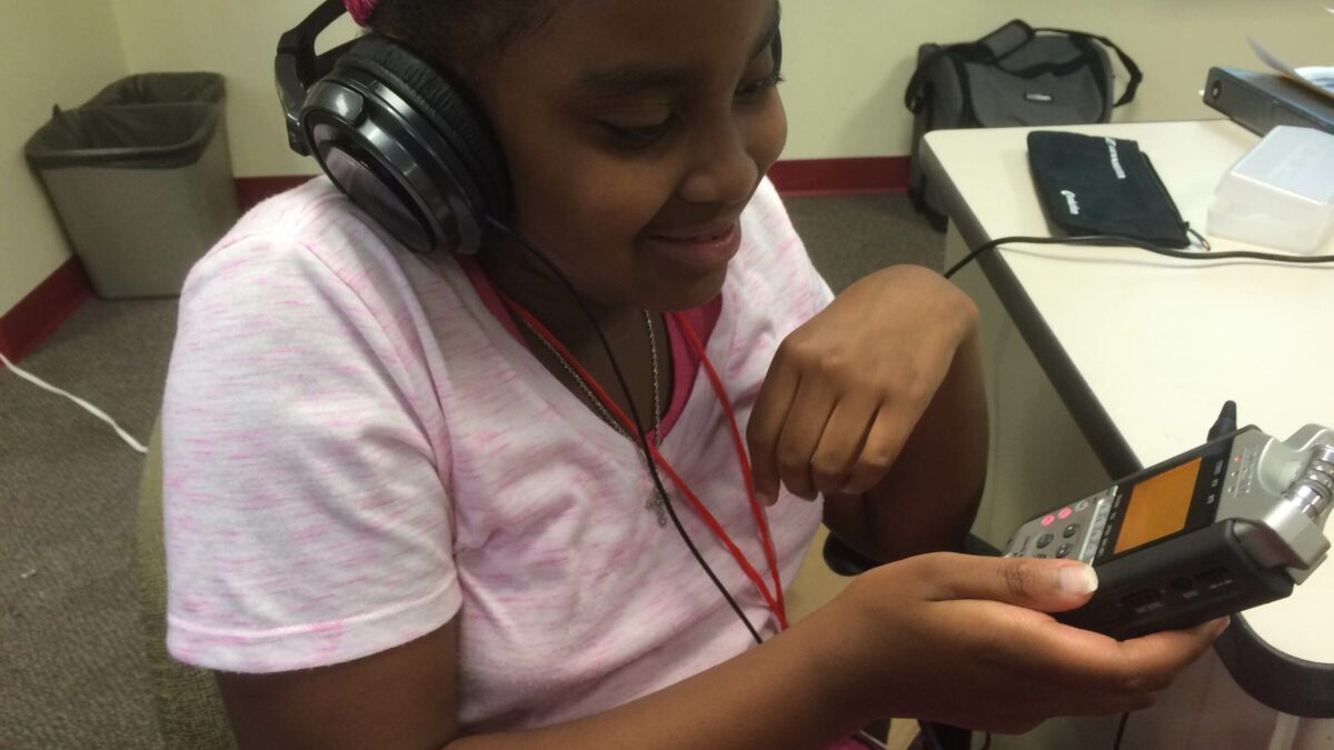 A youth wearing headphones looking down at a portable recorder in a classroom