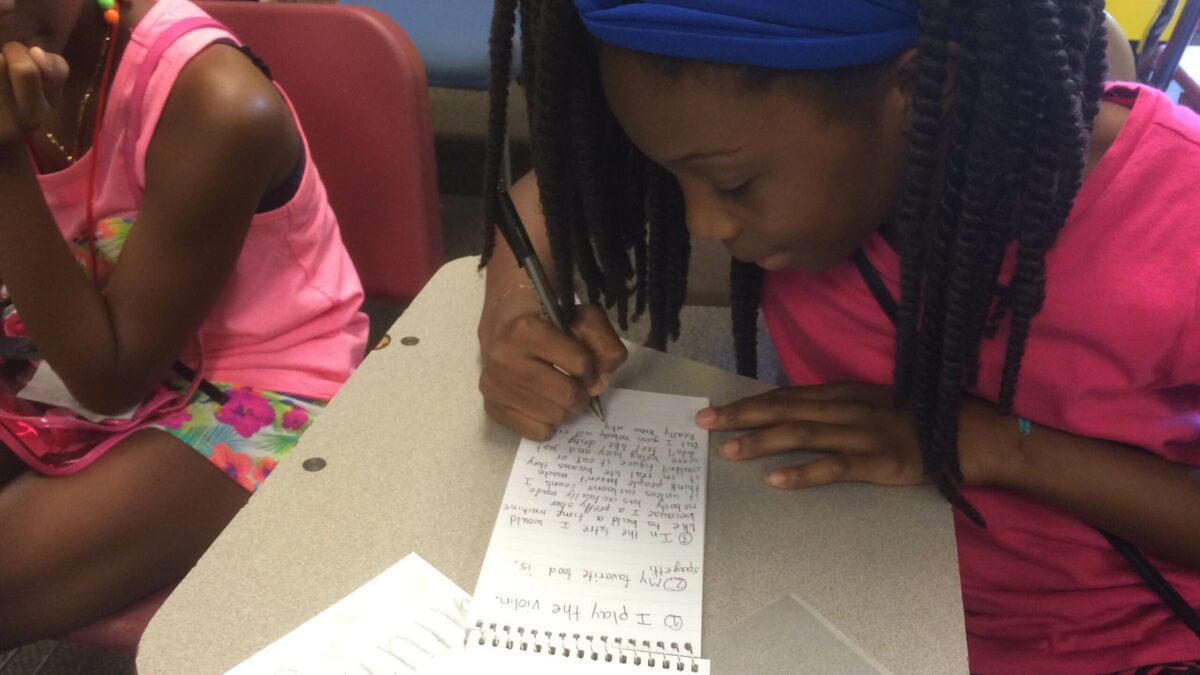 A youth writing onto a notepad sitting at a classroom desk