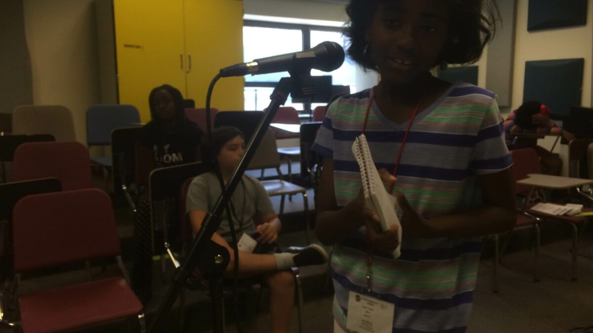 IMG_2975 A youth holding a notepad speaking into a microphone in a classroom