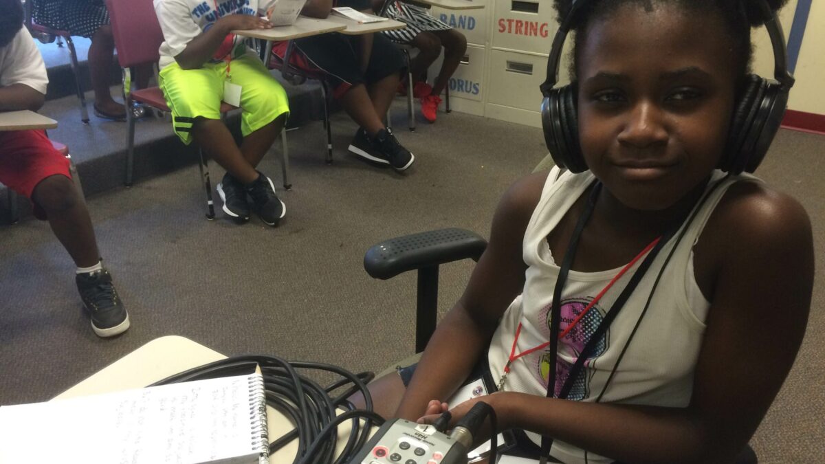 IMG_2985 A youth wearing headphones sitting behind a portable microphone and a notepad on a desk in a classroom