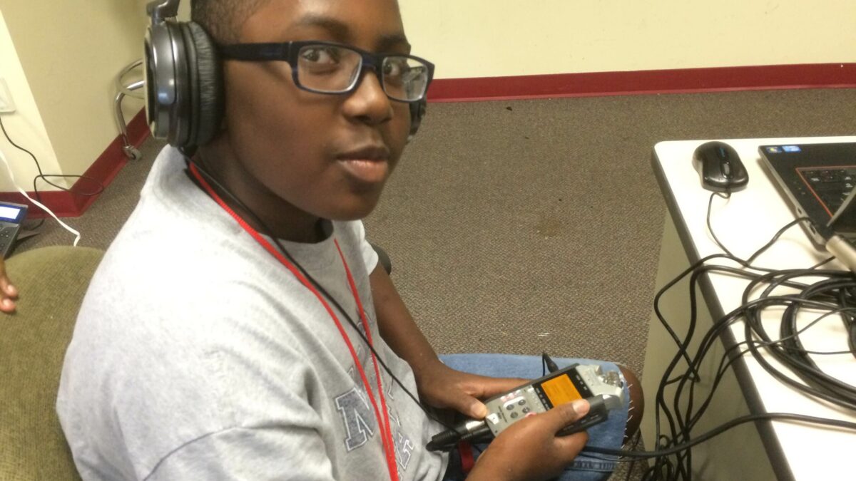 IMG_3001 A youth wearing headphones holding a portable recorder sitting next to a laptop computer