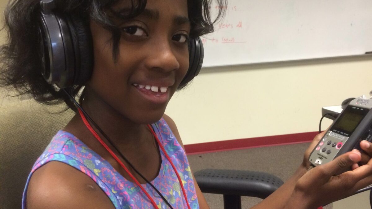 IMG_3003 A youth wearing headphones holding a portable recorder sitting in a classroom