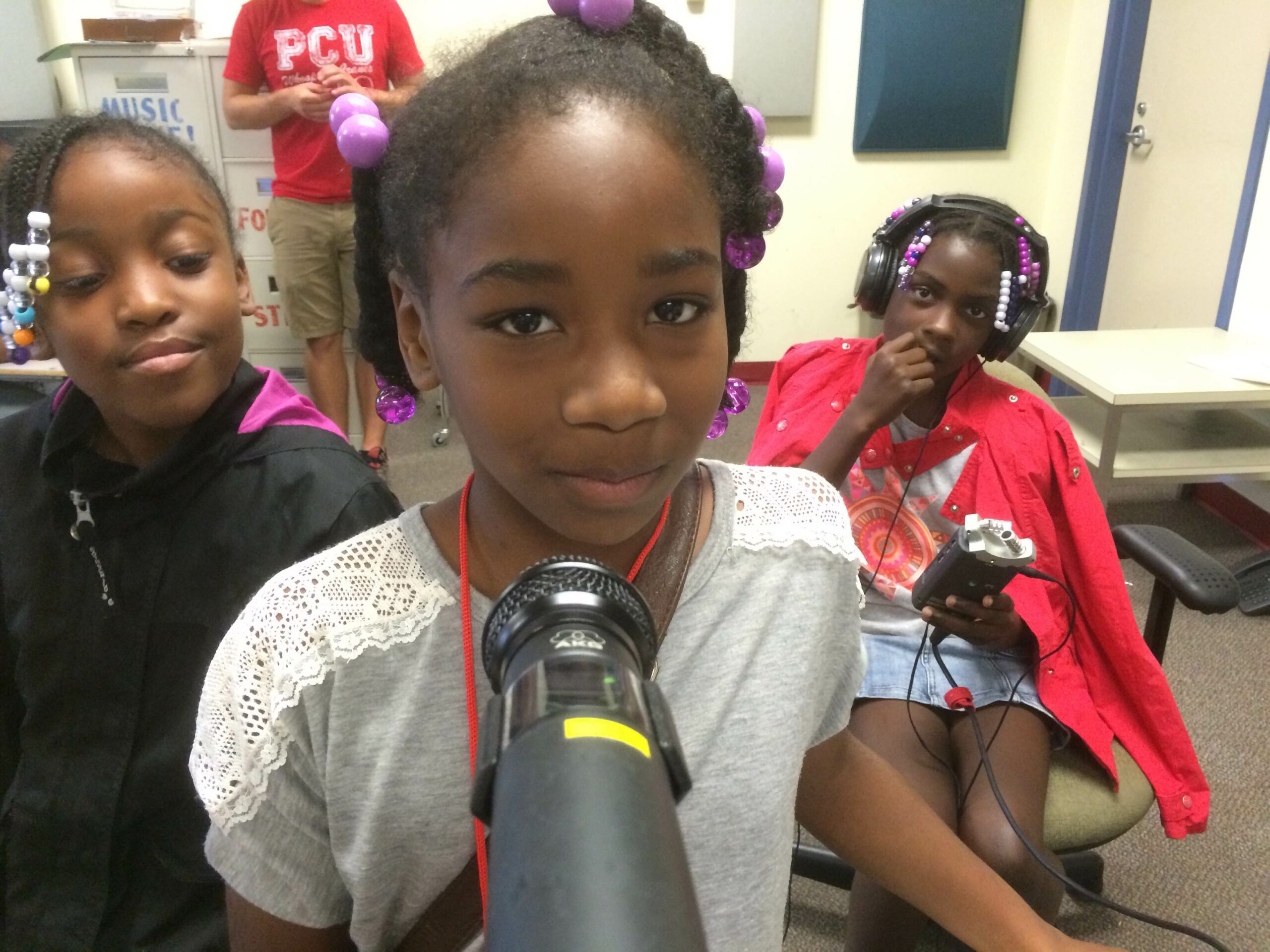 A youth standing behind a microphone, a youth standing and smiling, and a youth wearing headphones sitting and holding a portable recorder
