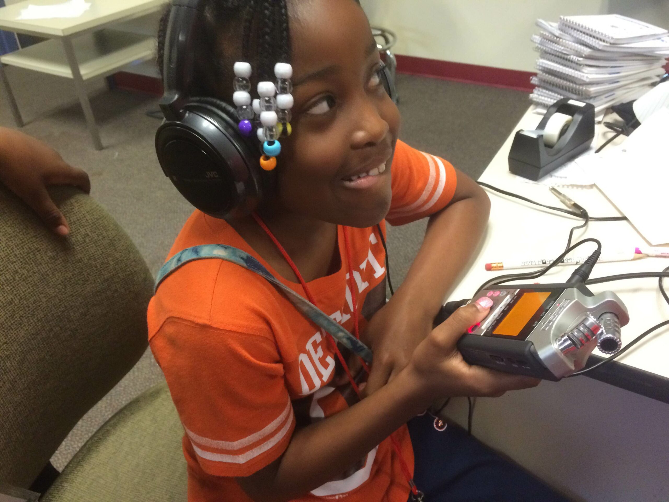A youth wearing headphones holding a portable recorder and smiling
